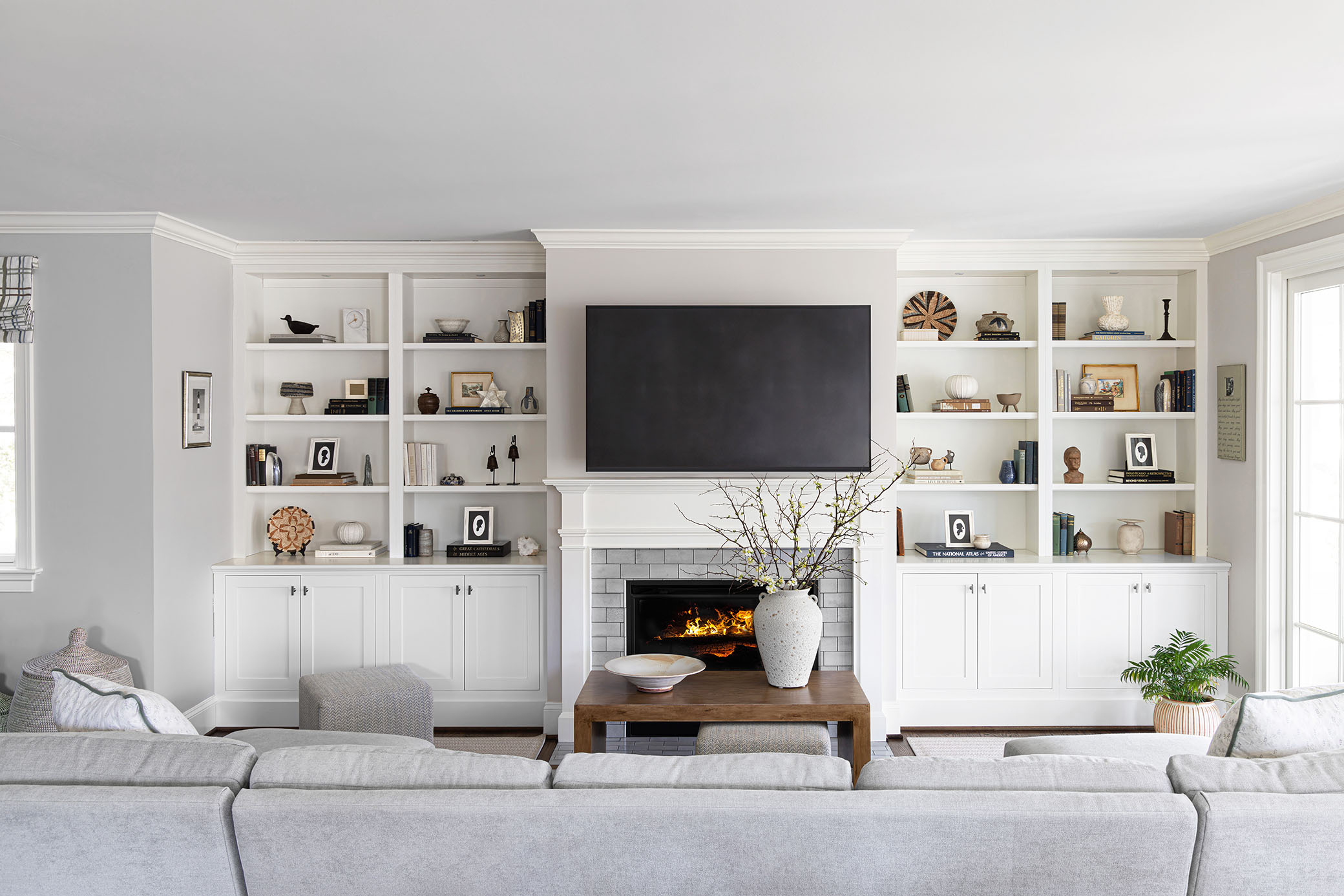 Chevy Chase MD living room with symmetrical floor-to-ceiling white built-in bookcases, fireplace hearth, TV, and neutral sectional sofa by interior photographer