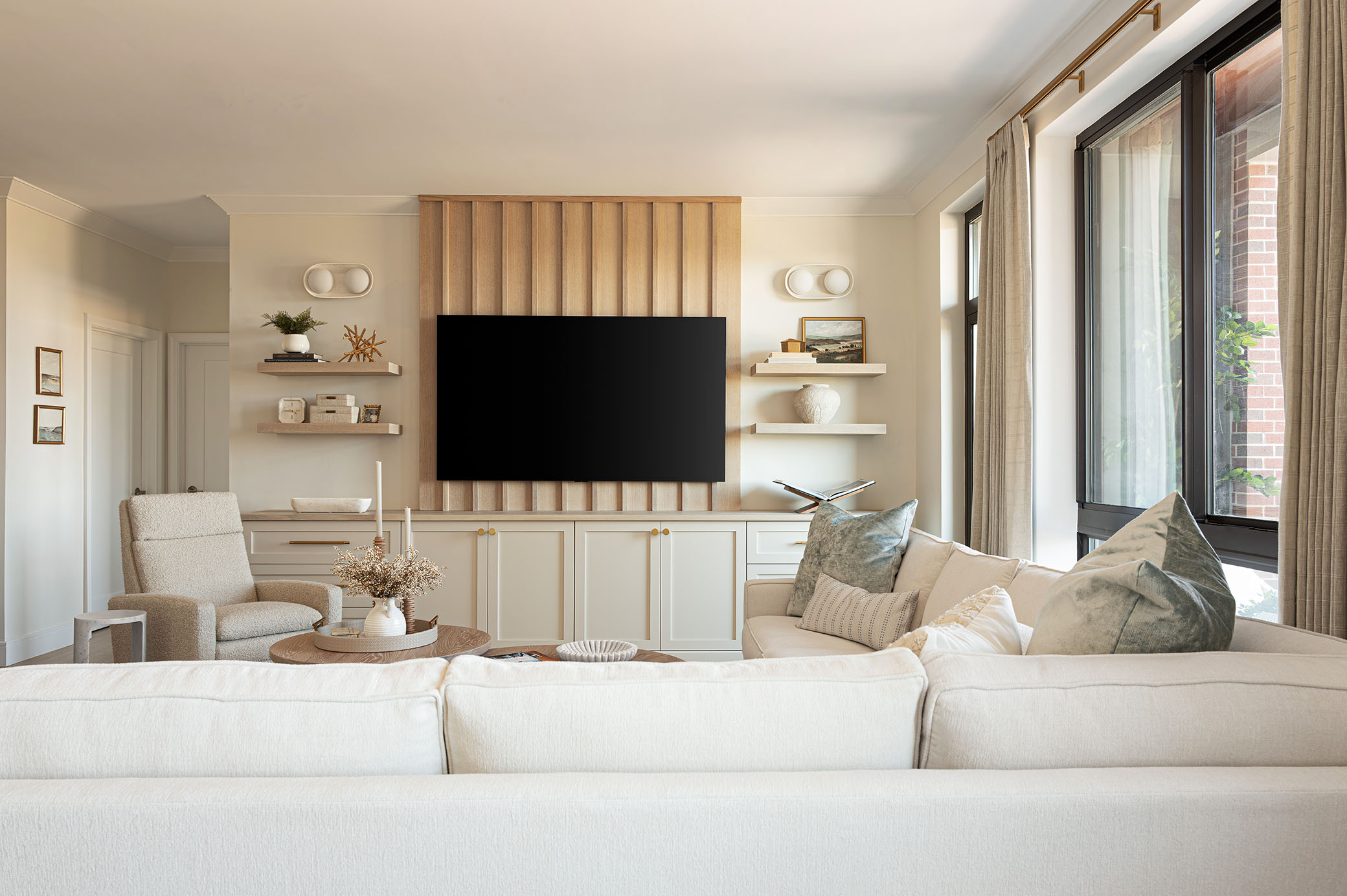 Modern luxury apartment living room featuring vertical slatted wood TV feature wall, cream sectional, and custom built-in shelving captured by interior architectural photographer