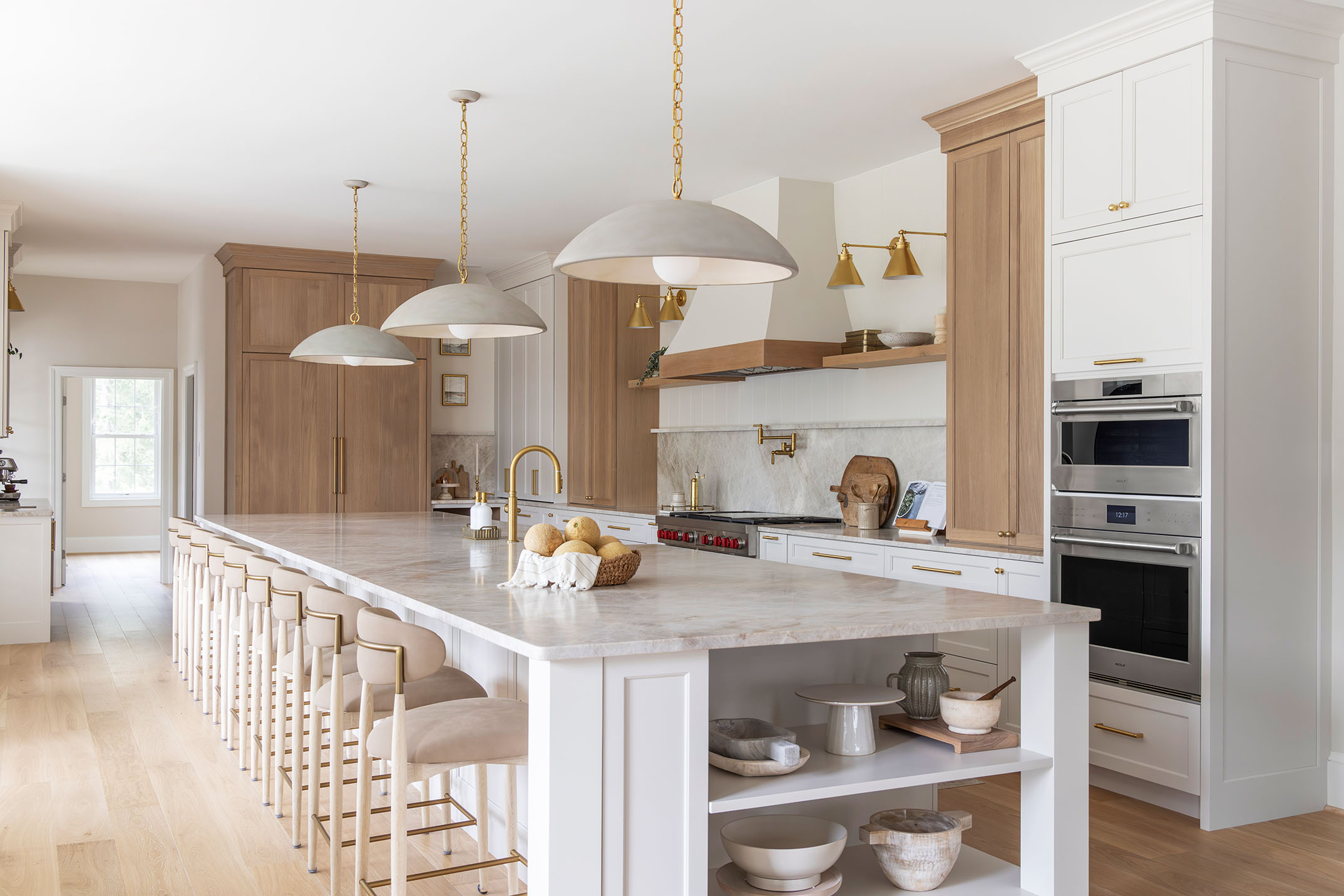 Luxury kitchen featuring expansive white marble waterfall island, natural warm oak cabinetry, and brass dome pendant lighting by kitchen photographer DC MD VA