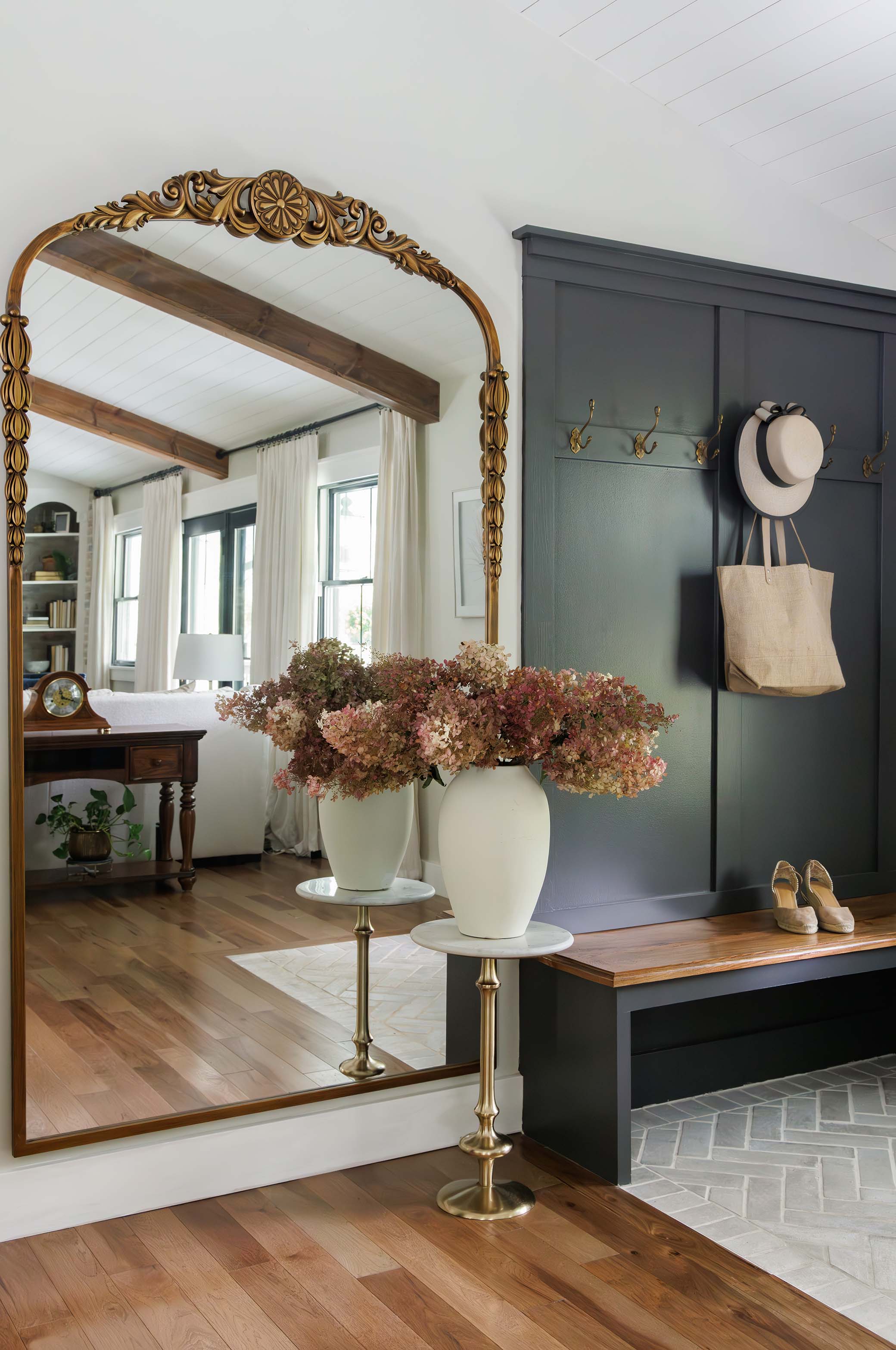 Montgomery County MD interior foyer vignette featuring grand gold arched floor mirror, marble pedestal tables, dried hydrangeas, and dark grey paneling