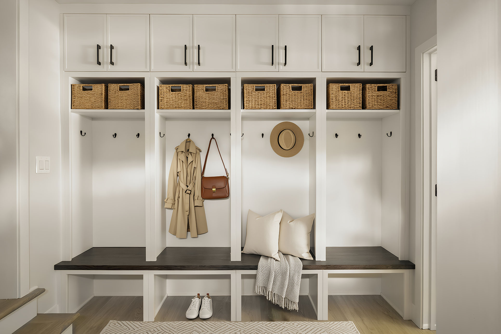 North Bethesda MD custom white mudroom built-in storage cubbies, dark wooden seating bench, and woven baskets photographed by interior architectural photographer