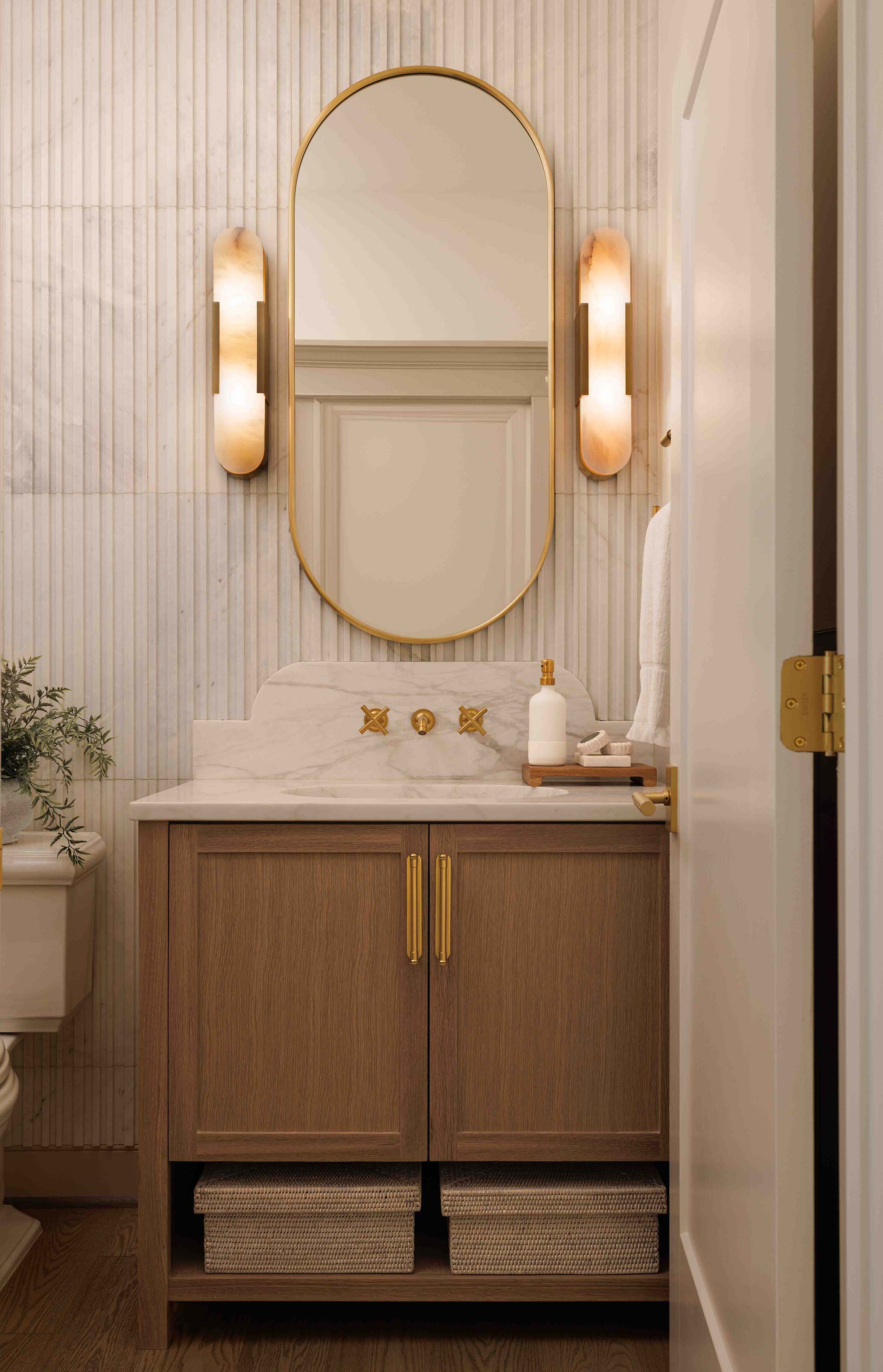 Northern Virginia powder room vanity with vertical fluted marble wall tiles, oval gold mirror, and alabaster wall sconces by NOVA interior photographer