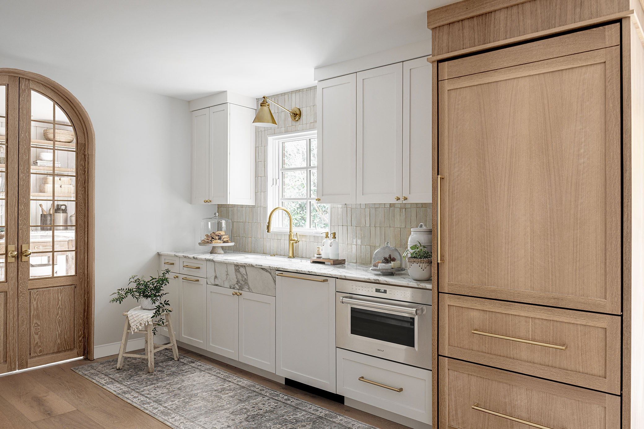 Luxury white and oak kitchen in Potomac MD featuring marble counter, glazed vertical tile backsplash, brass fixtures, and custom arched wood glass doors photographed by interior photographer